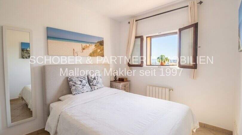 Bright bedroom with white double bed, ocean view picture and window with view in Son Servera
