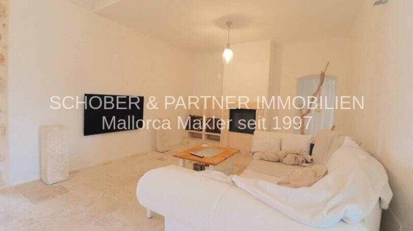 Helles Wohnzimmer mit weißem Sofa, Holztisch, TV und Gewölbedecke im sanierten Landhaus in Port de Manacor