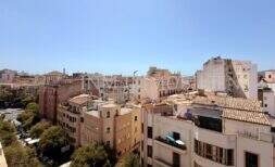 Panoramablick über die Altstadt von Palma de Mallorca mit historischen Gebäuden und Terrakotta-Dächern bei blauem Himmel.