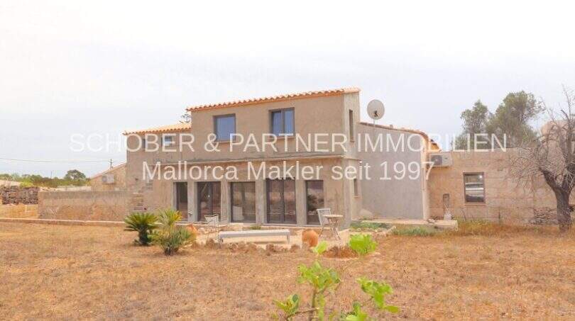 Außenansicht eines sanierten Landhauses in Portocristo mit Terrassenfläche, Satellitenantenne und trockenem Gartengrundstück.