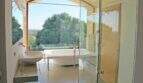 Luxuriöses Designerbad der Finca Felanitx mit freistehender Wanne, Glasdusche und Panoramafenster zum Grün.