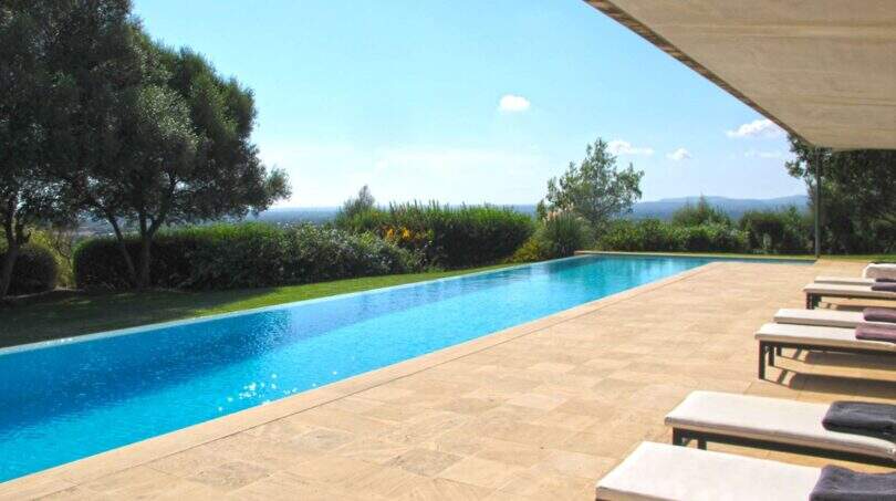 Weitläufiger Infinity-Pool der Designer-Finca in Felanitx mit Natursteintetrasse, Liegestühlen und Panoramablick ins Grüne.