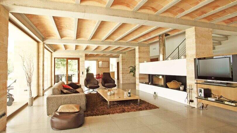 Helles Wohnzimmer der Designer-Finca in Felanitx mit Gewölbedecke, Kamin, modernen Sesseln und großen Fensterfronten.