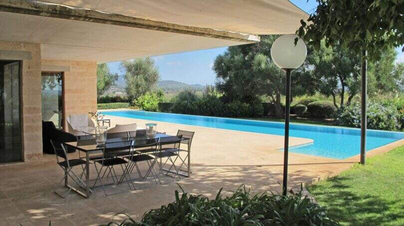 Überdachte Terrasse mit Esstisch und großem Pool der Designer-Finca in Felanitx, Blick auf grüne Landschaft