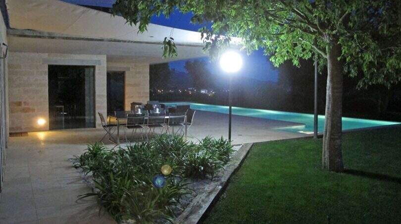 Beleuchteter Außenbereich der Designer-Finca bei Nacht mit Terrasse, Esstisch und beleuchtetem Infinity-Pool in Felanitx
