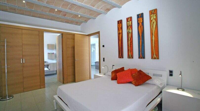 Helles Schlafzimmer der Designer-Finca Felanitx mit weißem Doppelbett, orangefarbenen Kissen und Gewölbedecke.
