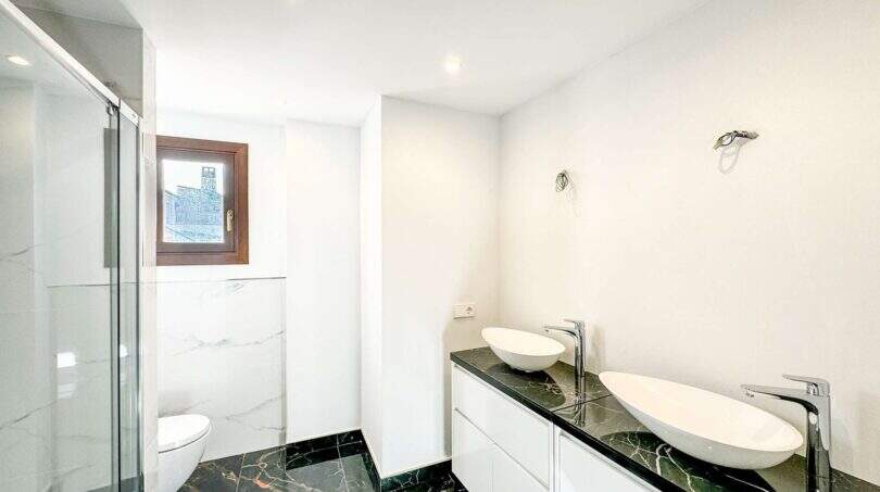 Baño moderno del apartamento de lujo en Felanitx con lavabo doble sobre mármol negro y ducha de cristal.