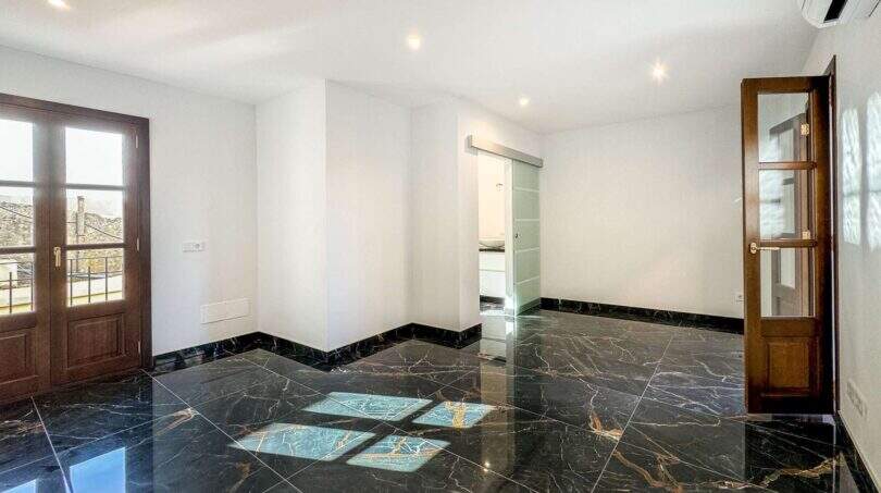 Sala de estar vacía con suelos de mármol negro pulido, paredes blancas y puertas de madera en apartamento de lujo en Felanitx