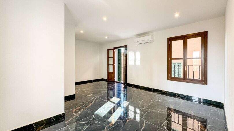 Sala de estar vacía del apartamento de lujo en Felanitx con suelos de mármol negro, aire acondicionado y ventanas de madera