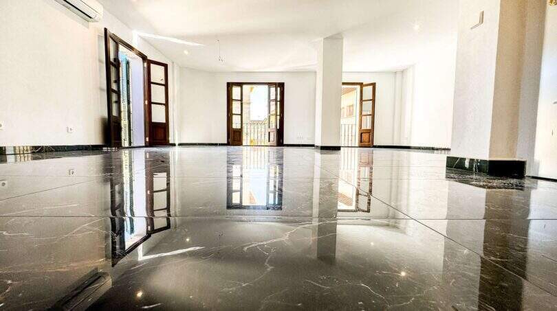 Sala de estar vacía con suelos de mármol negro pulido brillante y tres puertas balconeras de madera en apartamento de lujo en Felanitx
