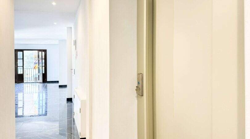 Pasillo luminoso del apartamento de lujo en Felanitx con suelos de mármol, paredes blancas y vista hacia la puerta de entrada con balcón.