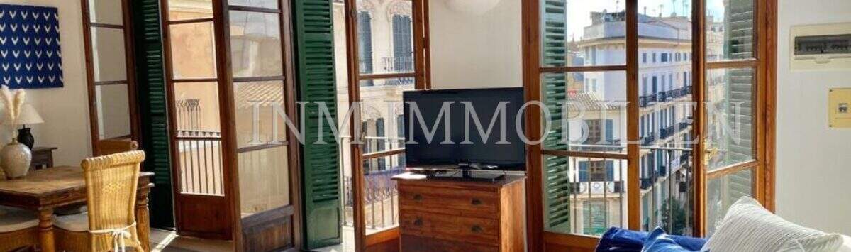 Luminosa sala de estar con sofá blanco, muebles de madera y grandes puertas de balcón con contraventanas verdes en Palma