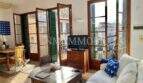 Luminosa sala de estar con sofá blanco, muebles de madera y grandes puertas de balcón con contraventanas verdes en Palma
