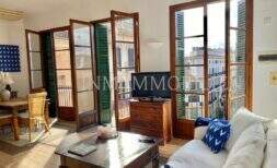Helles Wohnzimmer mit weißem Sofa, Holzmöbeln und großen Balkontüren mit grünen Fensterläden in Palma