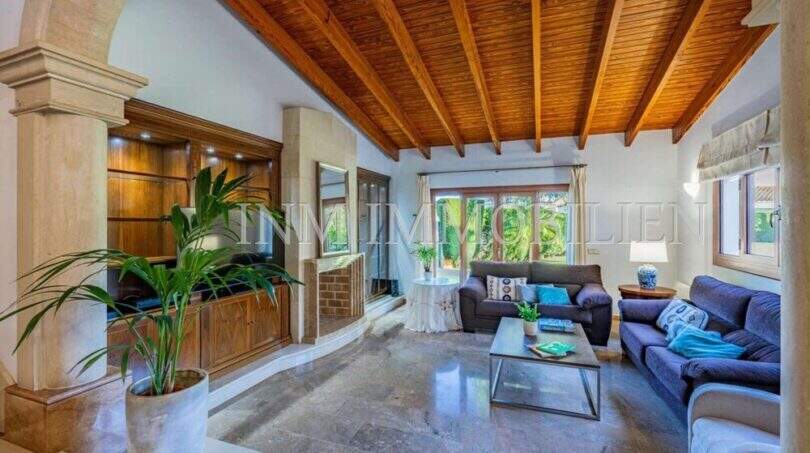 Wohnzimmer mit Holzbalkendecke, Marmorböden, blauen Sofas und Blick in den Garten – mediterrane Villa Sa Coma