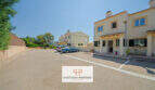 Außenansicht Reiheneckhaus Porto Cristo Novo: Parkplatz, mediterrane Fassade, Terrasse mit Gartenmöbeln, blauer Himmel.