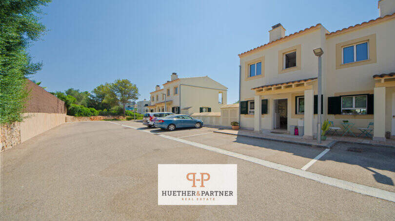 Außenansicht Reiheneckhaus Porto Cristo Novo: Parkplatz, mediterrane Fassade, Terrasse mit Gartenmöbeln, blauer Himmel.