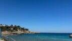 Türkisblaues Meer und felsige Küste in Cala Murada mit weißer Villa auf der Klippe und klarem Himmel.