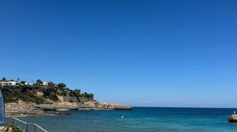 Türkisblaues Meer und felsige Küste in Cala Murada mit weißer Villa auf der Klippe und klarem Himmel.