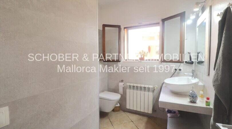 Modern bathroom in Son Servera with wall-mounted toilet, sink, radiator and window.