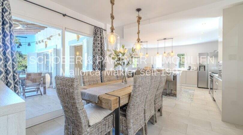 Eleganter Essbereich mit Rattanstühlen, Holztisch und offener Küche, Blick auf sonnige Terrasse in mediterraner Villa Sa Coma
