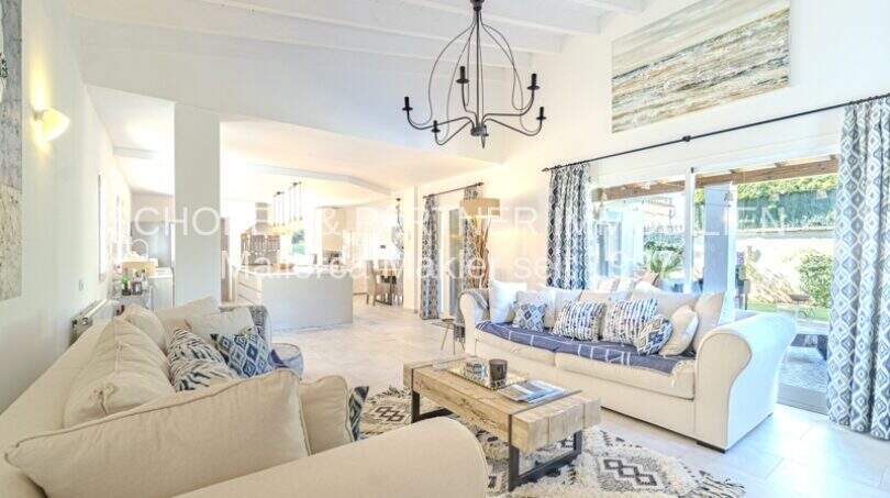 Helles Wohnzimmer der mediterranen Villa in Sa Coma mit Sofas, Kronleuchter und Gartenblick.