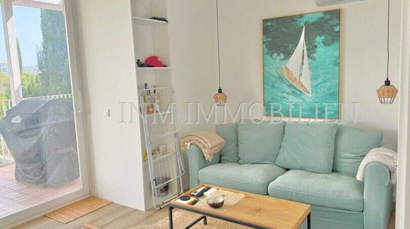 Helles Wohnzimmer mit türkisfarbenem Sofa, Segelboot-Kunstwerk und Balkonzugang in Cala d'Or