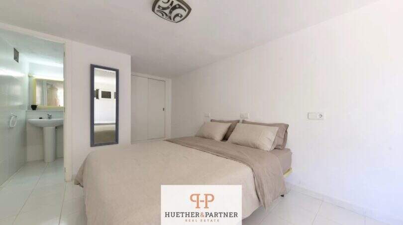 Helles Schlafzimmer der Erdgeschosswohnung in Cala Mandía mit Doppelbett, En-suite-Bad und weißen Fliesen.
