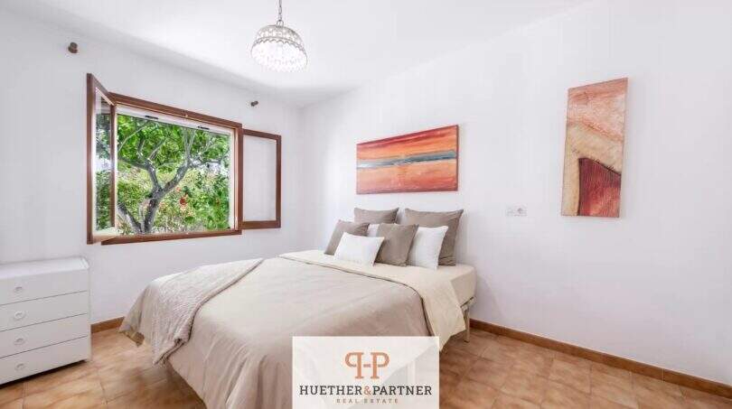 Helles Schlafzimmer der Erdgeschosswohnung in Cala Mandía mit Doppelbett, Terrakottaboden und Gartenblick.