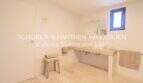 Helles Badezimmer mit cremefarbenem Natursteinboden, modernem Waschtisch und kleinem Holzhocker im sanierten Landhaus Portocristo