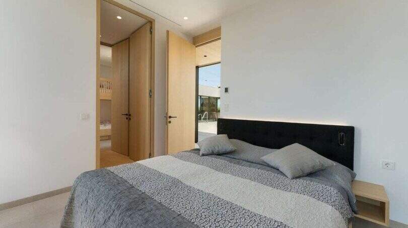Modern bedroom with black upholstered headboard, gray bedding and access to terrace in design villa S'Alqueria Blanca