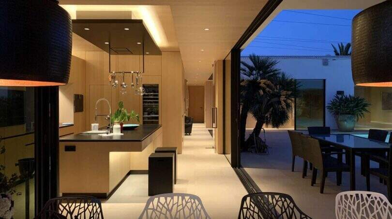 Open kitchen-living area with cooking island, design chairs and transition to illuminated terrace at night