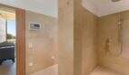 Modern bathroom with beige natural stone tiles, accessible shower with rain shower head and view of the terrace.