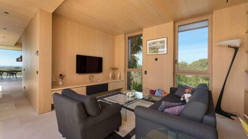 Bright living room with wooden cladding, TV, sofas and panoramic windows with sea view in S'Alqueria Blanca