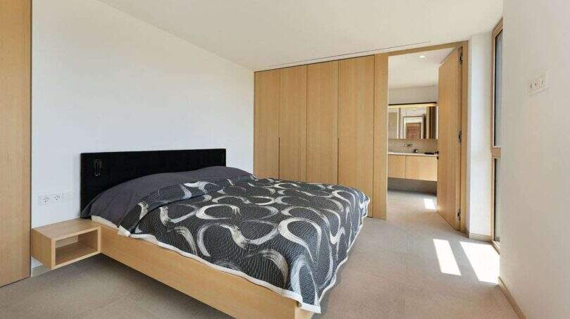Modern bedroom with double bed, wooden built-in wardrobe and adjoining bathroom in design house Mallorca.