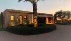 Exterior view design house S'Alqueria Blanca at sunset with palm, circular path and warm light ambiance.