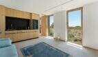 Bright living room with wooden kitchen, blue carpet and panoramic windows with view of Mediterranean landscape