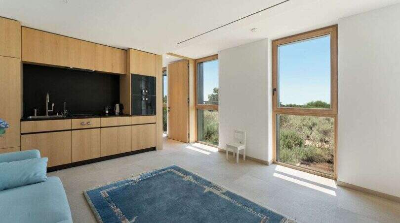 Bright living room with wooden kitchen, blue carpet and panoramic windows with view of Mediterranean landscape