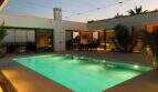Illuminated outdoor pool at dusk, surrounded by modern white facade with panoramic glazing in S'Alqueria Blanca.