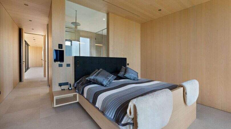 Modern bedroom with wooden cladding, black headboard, striped bedding and open shower area in S'Alqueria Blanca.