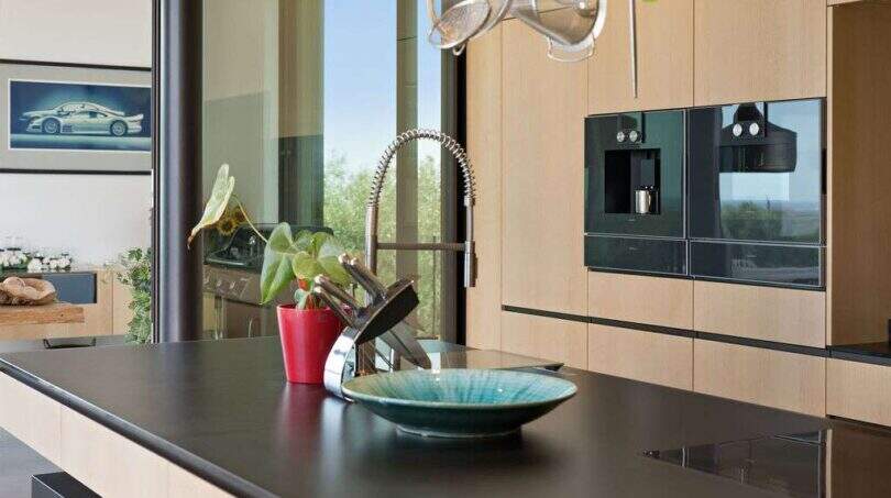Modern designer kitchen with black granite island, built-in appliances and large windows with nature view