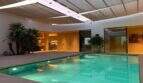 Indoor pool area with turquoise water, palms and modern living access in designer villa S'Alqueria Blanca