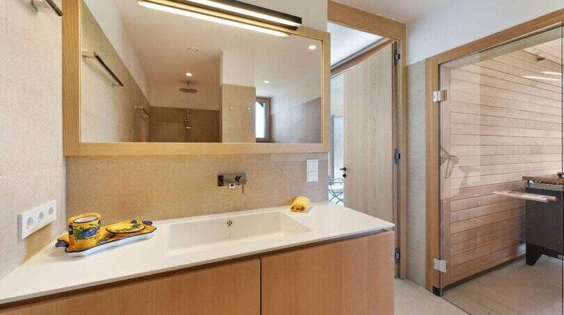 Modern bathroom with wooden vanity, illuminated mirror and sauna in design house S'Alqueria Blanca