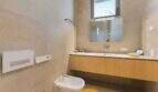 Modern bathroom with bidet, floating wooden vanity, wall mirror and beige natural stone walls in design house S'Alqueria Blanca