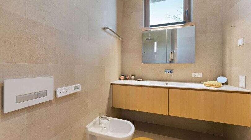 Modern bathroom with bidet, floating wooden vanity, wall mirror and beige natural stone walls in design house S'Alqueria Blanca