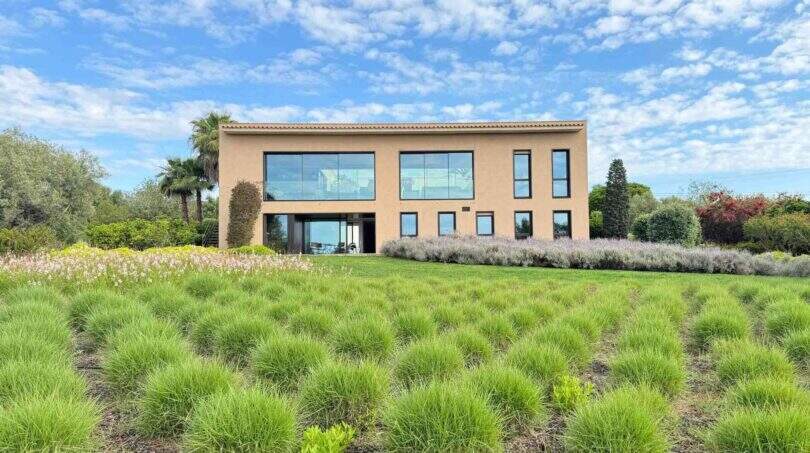 Exterior view modern design house S'Alqueria Blanca with large glass fronts, lush garden and lavender beds