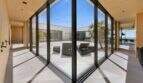 Light-filled glass corridor with view of courtyard terrace with lounge chairs and sea view in modern design house