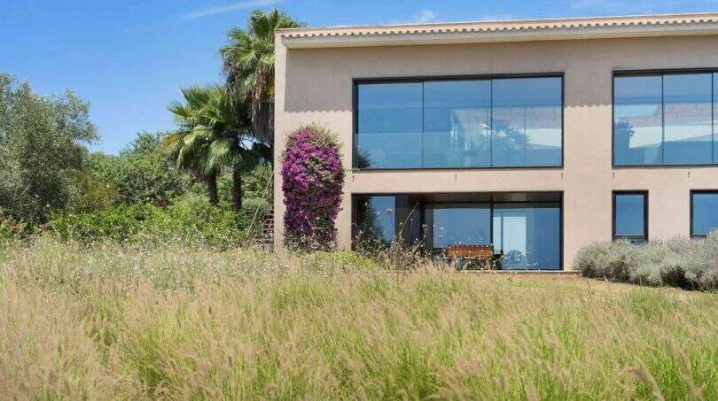 Exterior view modern design house S'Alqueria Blanca with bougainvillea, palm and large glass fronts
