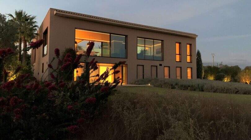 Modern design house in S'Alqueria Blanca at dusk with illuminated interior and Mediterranean garden.