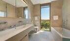Modern bathroom with double sink, bathtub, bidet and large window with green view in design villa.